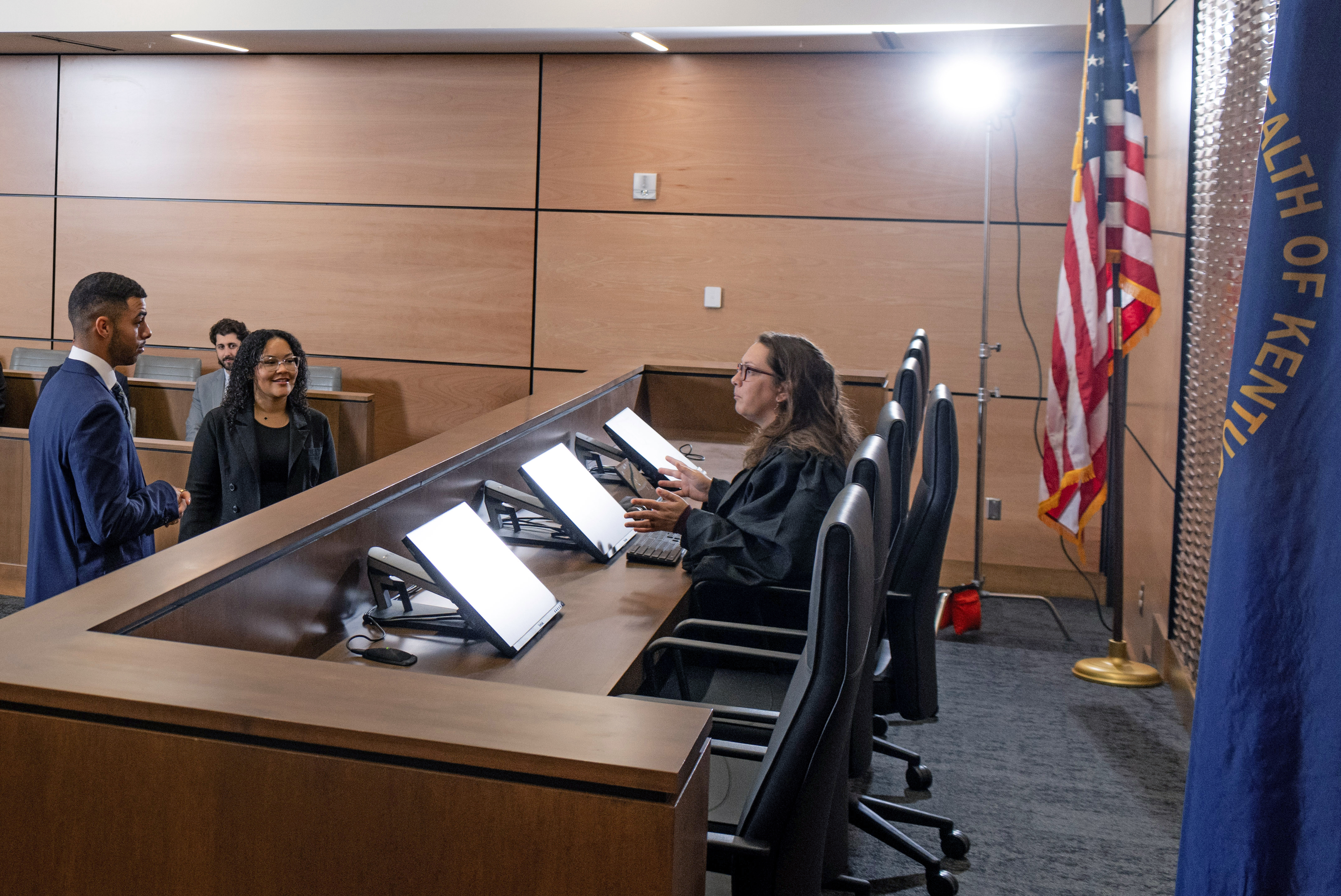 Three students in the Foundation Courtroom at the judge's bench