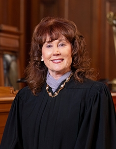 Smiling woman in a black judge’s robe standing in a courtroom.