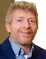 Head-and-shoulders portrait of a middle-aged man with light hair and a short beard, wearing a blue jacket and light blue shirt.