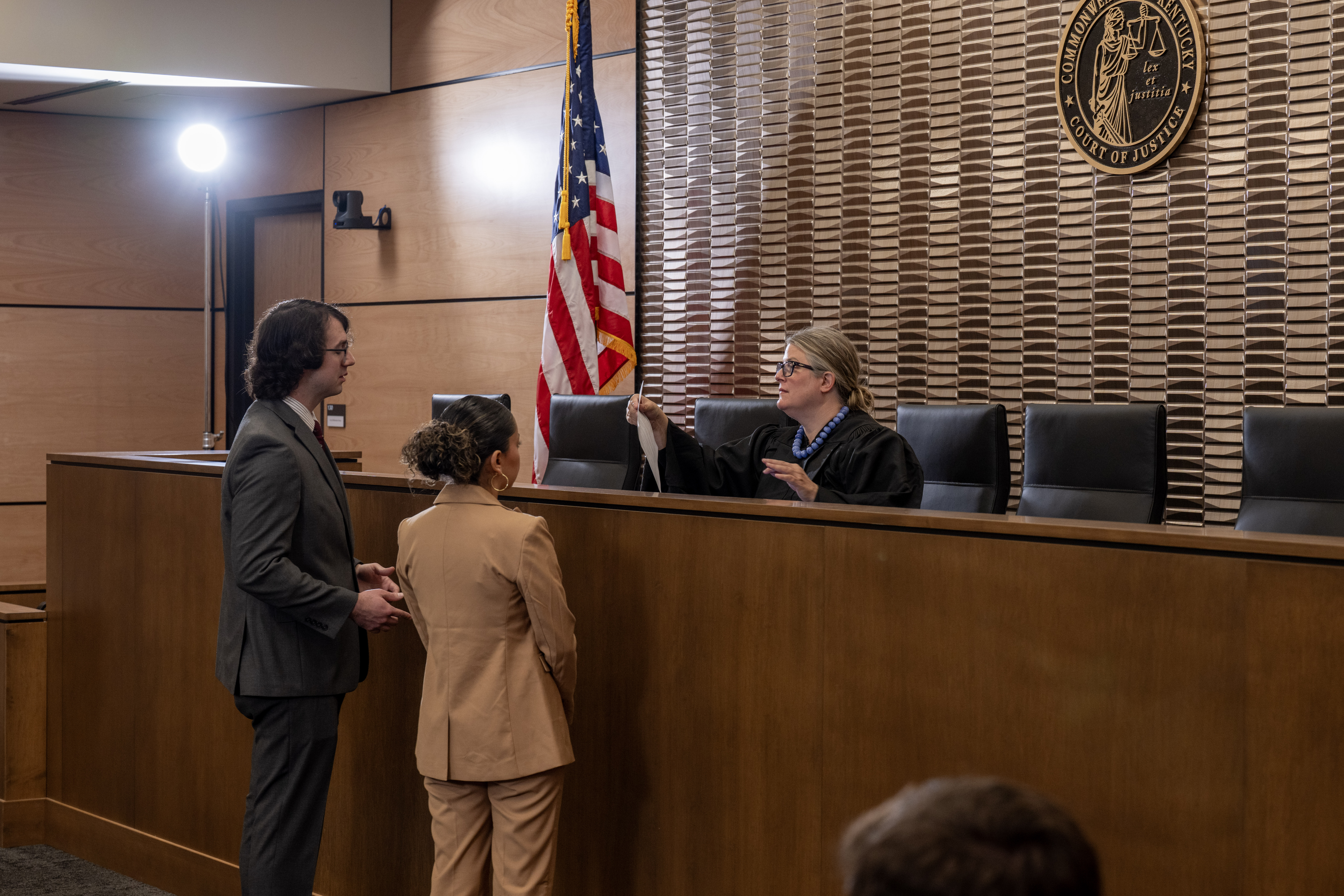 Two law students standing with a judge in the Foundation Courtroom at Chase Law School