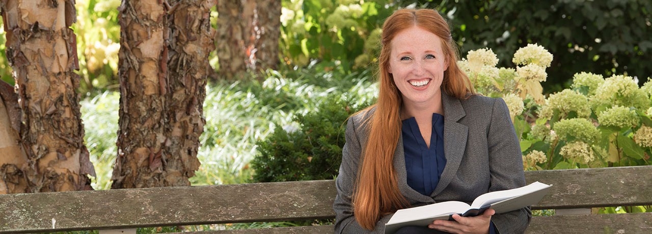 Young, professionally dressed woman smiling outdoors.